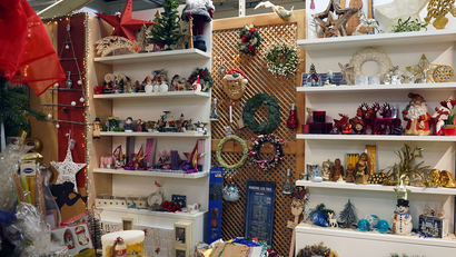 Auf dem Bild sind verschiedene weihnachtliche Dekorationsartikel und Accessoires zu sehen, die in Regalen und einem Korb arrangiert sind.