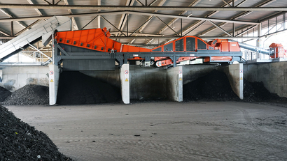 Auf dem Bild ist eine industrielle Anlage mit einem Förderband zu sehen, das vermutlich Materialien wie Kohle oder andere Rohstoffe transportiert und lagert.