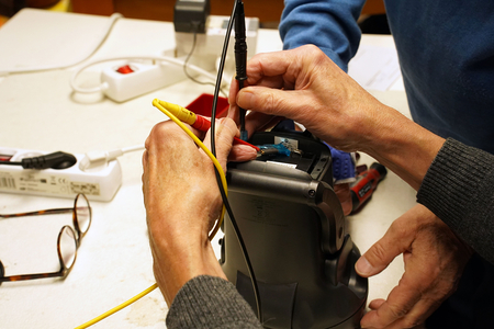 Auf dem Bild sind Hände zu sehen, die eine elektrische Komponente mit Testkabeln überprüfen oder reparieren.