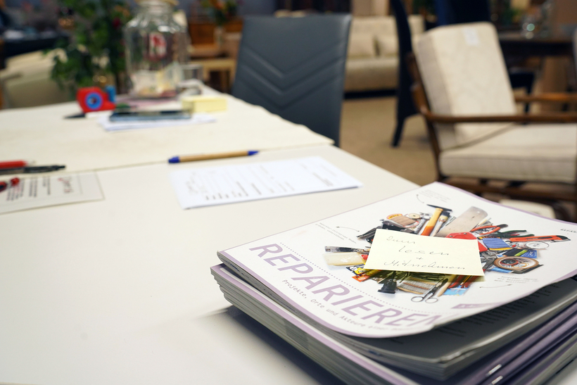 Auf dem Bild sind mehrere stapelbare Hefte mit dem Titel „REPARIEREN“ sowie Schreibmaterial auf einem Tisch zu sehen.