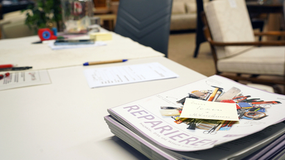 Auf dem Bild sind mehrere stapelbare Hefte mit dem Titel „REPARIEREN“ sowie Schreibmaterial auf einem Tisch zu sehen.