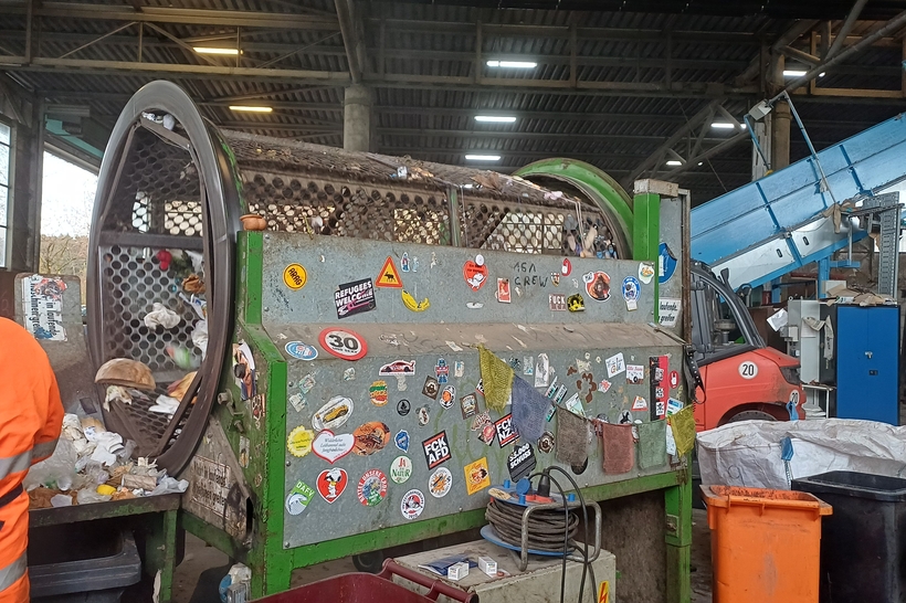 Das Bild zeigt eine recyclinganlage mit einem großen, mit Aufklebern bedeckten Maschinenraum, in dem Abfälle verarbeitet werden.