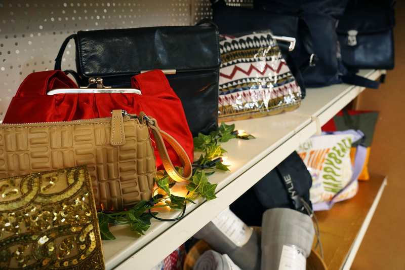 Auf dem Bild sind verschiedene Handtaschen und Taschen auf einem Regal zu sehen, umrahmt von grünen Pflanzen und Licht.