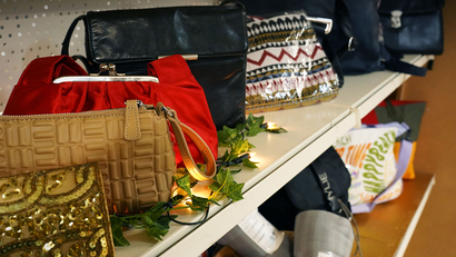 Auf dem Bild sind verschiedene Handtaschen und Taschen auf einem Regal zu sehen, umrahmt von grünen Pflanzen und Licht.