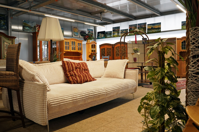 Auf dem Bild ist ein gemütliches Wohnzimmer mit einem weißen Sofa, einem Stehlampe, Pflanzen und verschiedenen Möbelstücken im Hintergrund zu sehen.