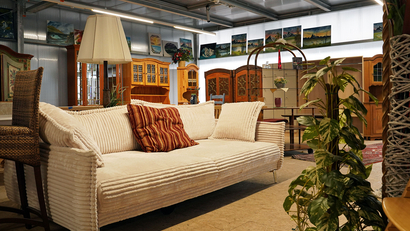 Auf dem Bild ist ein gemütliches Wohnzimmer mit einem weißen Sofa, einem Stehlampe, Pflanzen und verschiedenen Möbelstücken im Hintergrund zu sehen.