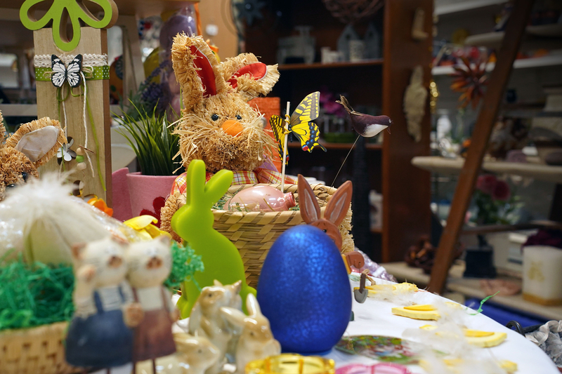 Auf dem Bild sind bunte Osterdekorationen zu sehen, darunter ein Strohhase, Eier und kleine Figuren.