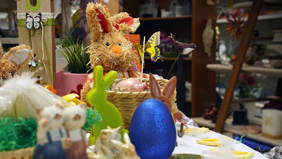 Auf dem Bild sind bunte Osterdekorationen zu sehen, darunter ein Strohhase, Eier und kleine Figuren.