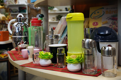 Auf dem Bild sind verschiedene Küchenutensilien und -gefäße, darunter Kannen, Gläser und Gewürzbehälter, auf einem Tisch angeordnet.