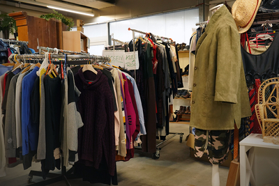 Auf dem Bild ist ein Second-Hand-Shop zu sehen, der mit Kleiderständern voller Kleidung und Accessoires ausgestattet ist.