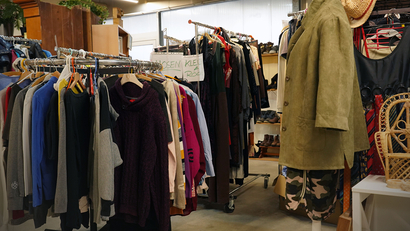 Auf dem Bild ist ein Second-Hand-Shop zu sehen, der mit Kleiderständern voller Kleidung und Accessoires ausgestattet ist.