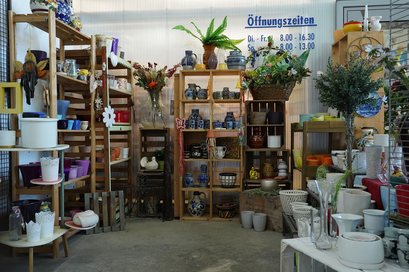 Das Bild zeigt einen Verkaufsbereich mit Regalen voller dekorativer Artikel, Töpfen und Vasen.