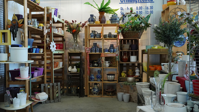 Das Bild zeigt einen Verkaufsbereich mit Regalen voller dekorativer Artikel, Töpfen und Vasen.