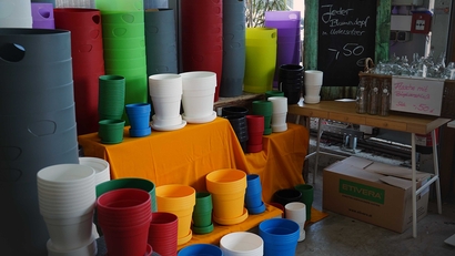 Auf dem Bild sind zahlreiche bunte Blumentöpfe und Pflanzgefäße in verschiedenen Größen und Farben zu sehen, die auf einem Tisch präsentiert werden.